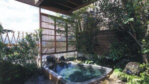 A stone hot tub in a garden with a wooden fence and lush greenery. - onjyuku yagura (Yufu)