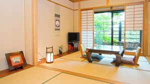 A traditional Japanese room with tatami flooring, a low table with cushions, a television, and a sliding door leading to a garden. - onjyuku yagura (Yufu)