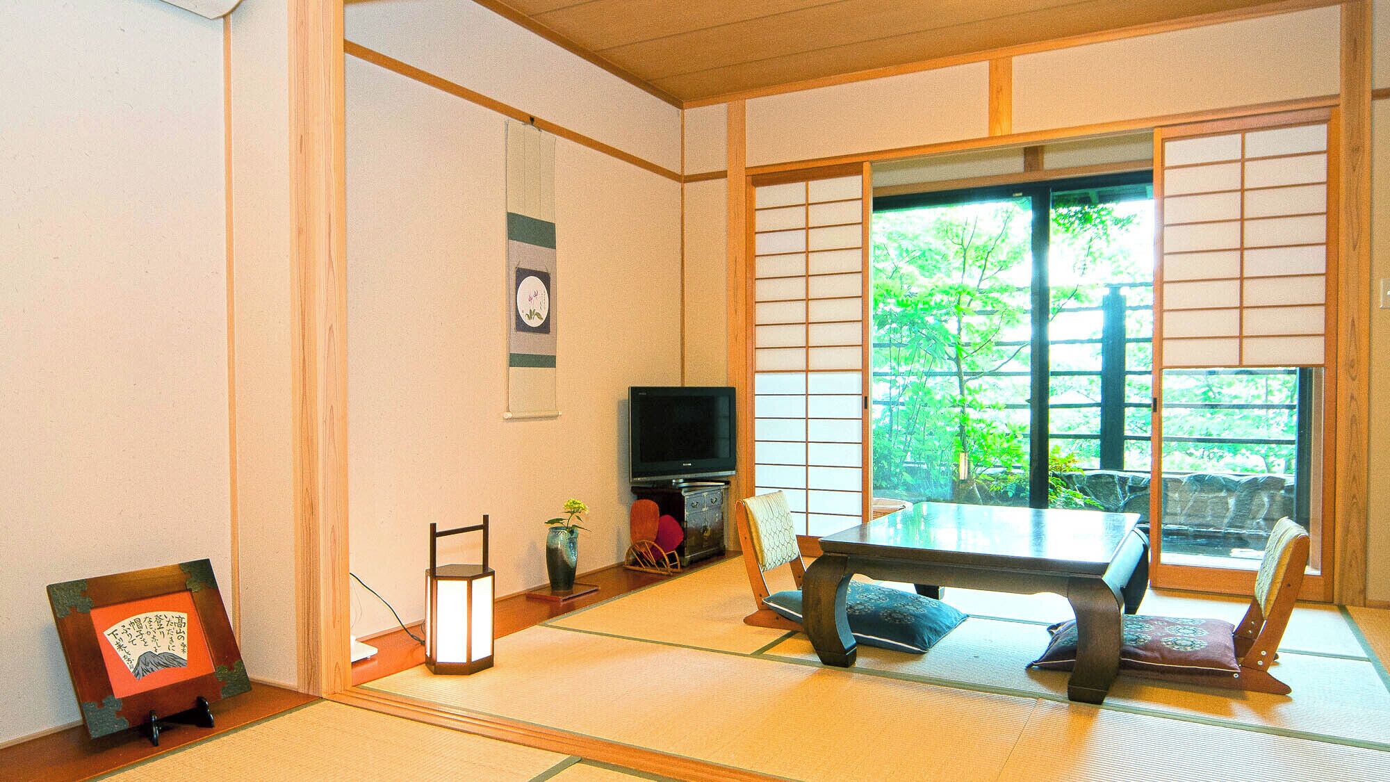 Une pièce de style japonais traditionnel, avec un sol recouvert de tatamis, une table basse, un téléviseur et une porte coulissante donnant sur un paysage verdoyant.