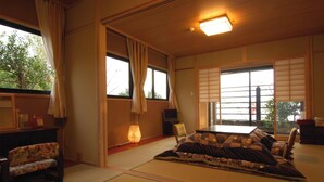 A traditional Japanese room with tatami flooring, a low table, a sofa, and a television. - onjyuku yagura (Yufu)