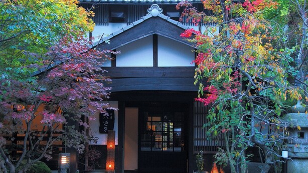 A traditional Japanese building with a tiled roof, a wooden entrance, and a stone lantern. - onjyuku yagura (Yufu)