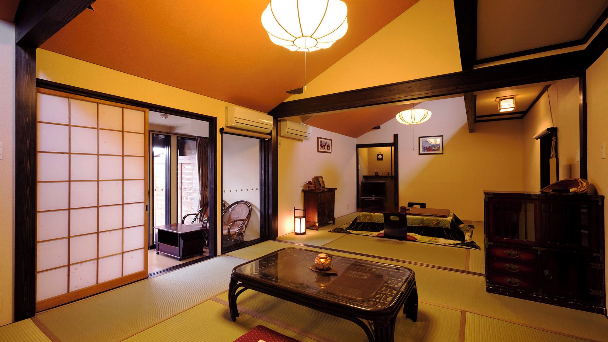Ein traditioneller japanischer Raum mit Tatami-Bodenbelag, einem niedrigen Tisch, einer Couch und Schiebetüren.
