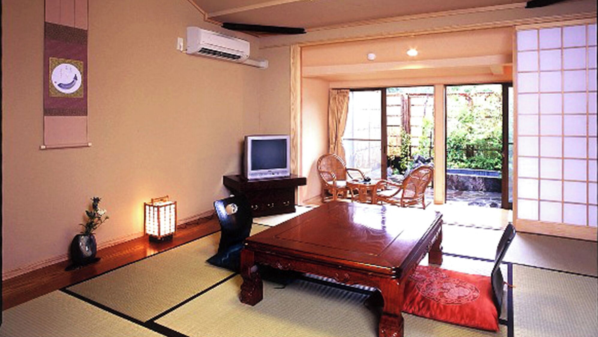 Ein traditioneller japanischer Raum mit Tatami-Böden, einem Fernseher auf einem Schrank und einer Schiebetür zu einem Außenbereich.