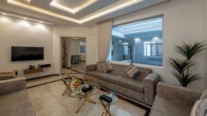 Een moderne woonkamer met een flatscreen-televisie, comfortabele banken, een glazen salontafel en een groot raam met uitzicht op het interieur.