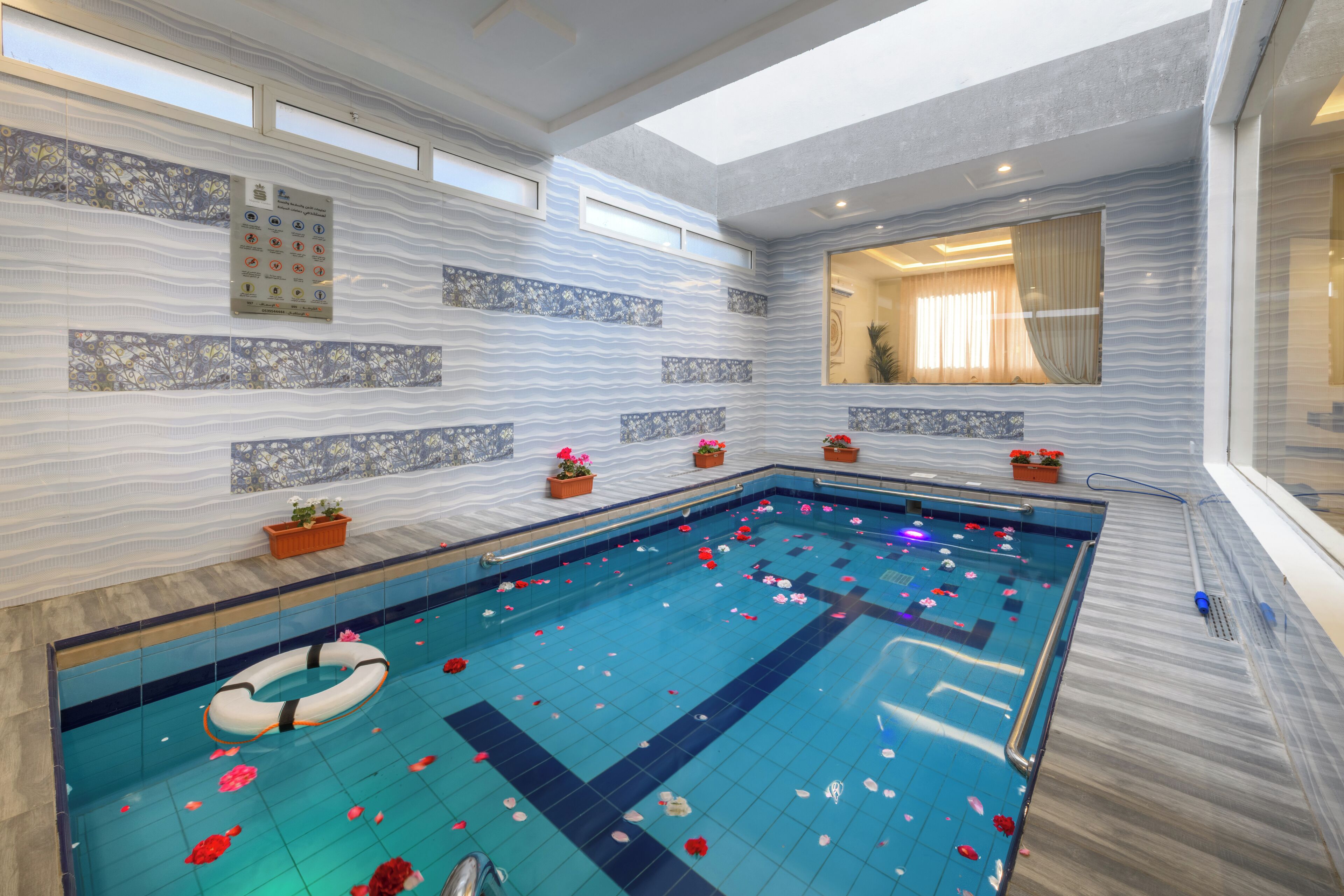 Un'ampia piscina al coperto con un galleggiante, piante in vaso e una parete piastrellata con motivo ondulato.
