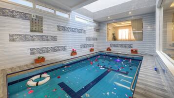 Un'ampia piscina al coperto con un galleggiante, piante in vaso e una parete piastrellata con motivo ondulato.