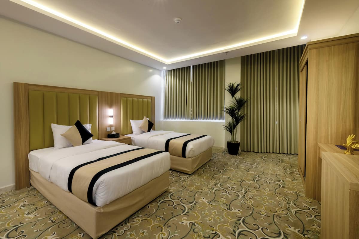 Ein Hotelzimmer mit zwei Betten, einem Nachttisch, einem Blumentopf und einem Holzschrank.