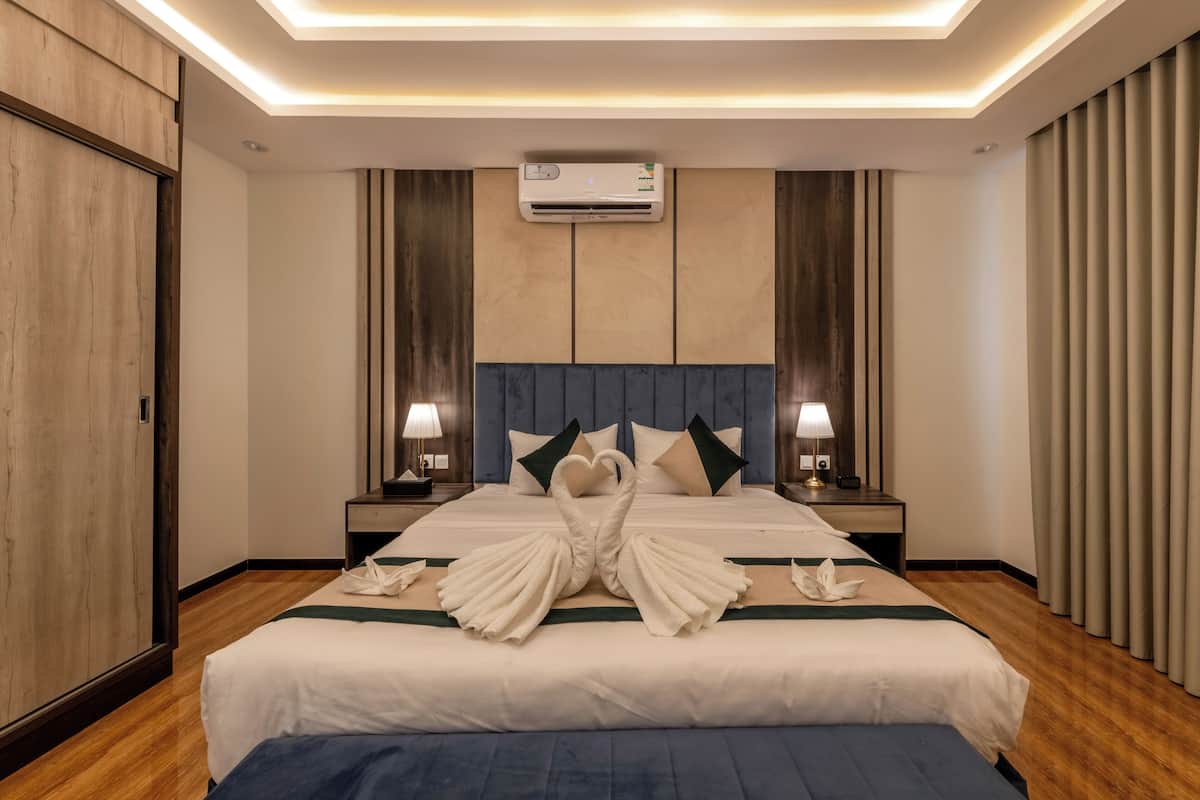 Ein Hotelzimmer mit einem großen Bett, zwei Nachttischen mit Lampen, einer Klimaanlage und einem Holzschrank.