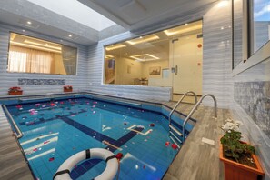 A modern indoor swimming pool with a clear glass wall, a lifebuoy, and a potted plant.