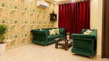 A spacious living room with two green sofas, a coffee table, a chandelier, ceiling fans, and a patterned wallpaper.