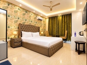 A hotel room with a large bed, a ceiling fan, a desk with a chair, and a television. - Ambient Express Cr Park (New Delhi)