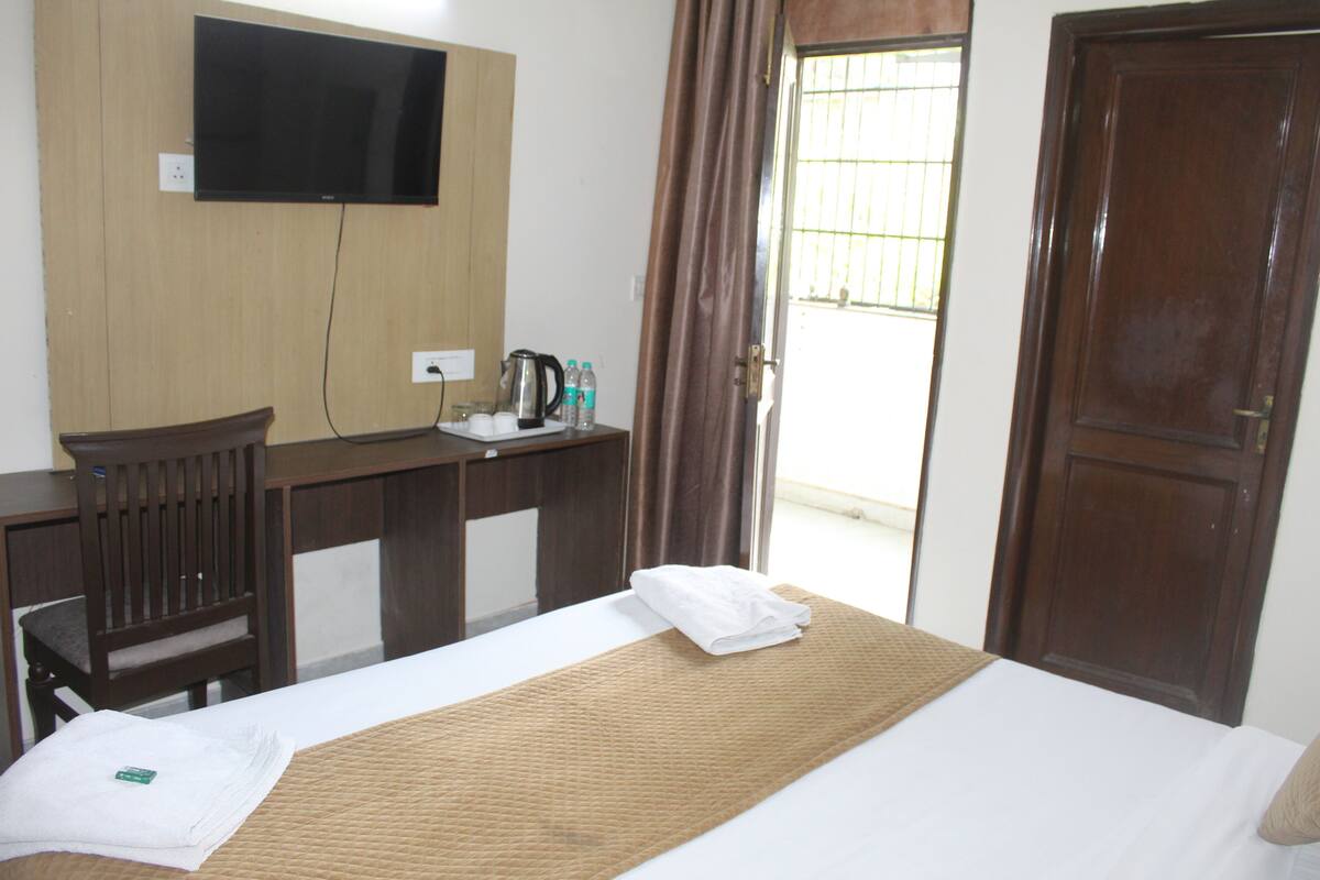A hotel room with a bed, a desk with a flat-screen TV, a kettle, and a window with curtains.