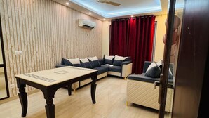 A modern living room with a sectional sofa, a coffee table, and a ceiling fan. - Ambient Express Cr Park (New Delhi)
