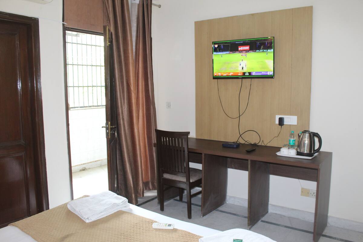 A hotel room with a bed, a desk, a TV mounted on the wall, a chair, and a window with curtains.