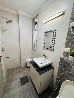 Un baño con ducha, lavamanos, espejo e inodoro.