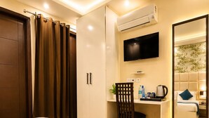 A hotel room with a bed, a desk, a chair, a television, and an air conditioning unit. - Ambient Express Cr Park (New Delhi)