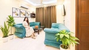 A living room with two sofas, a coffee table, a TV, and a ceiling fan. - Ambient Express Cr Park (New Delhi)