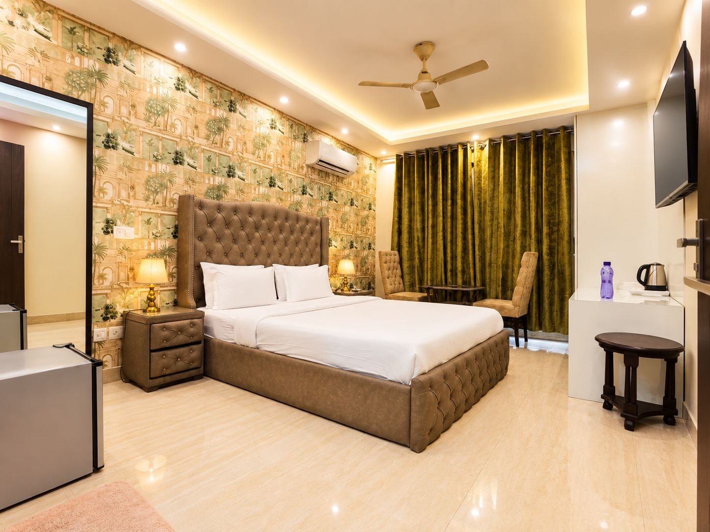 A hotel room with a large bed, a ceiling fan, a TV, and a minibar.
