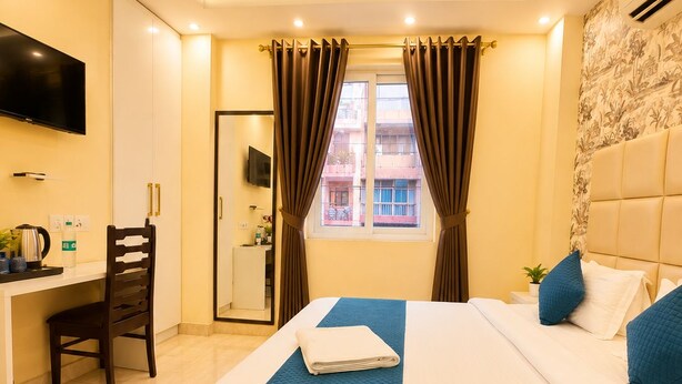A hotel room with a bed, a desk, a chair, a television, and a window with curtains. - Ambient Express Cr Park (New Delhi)