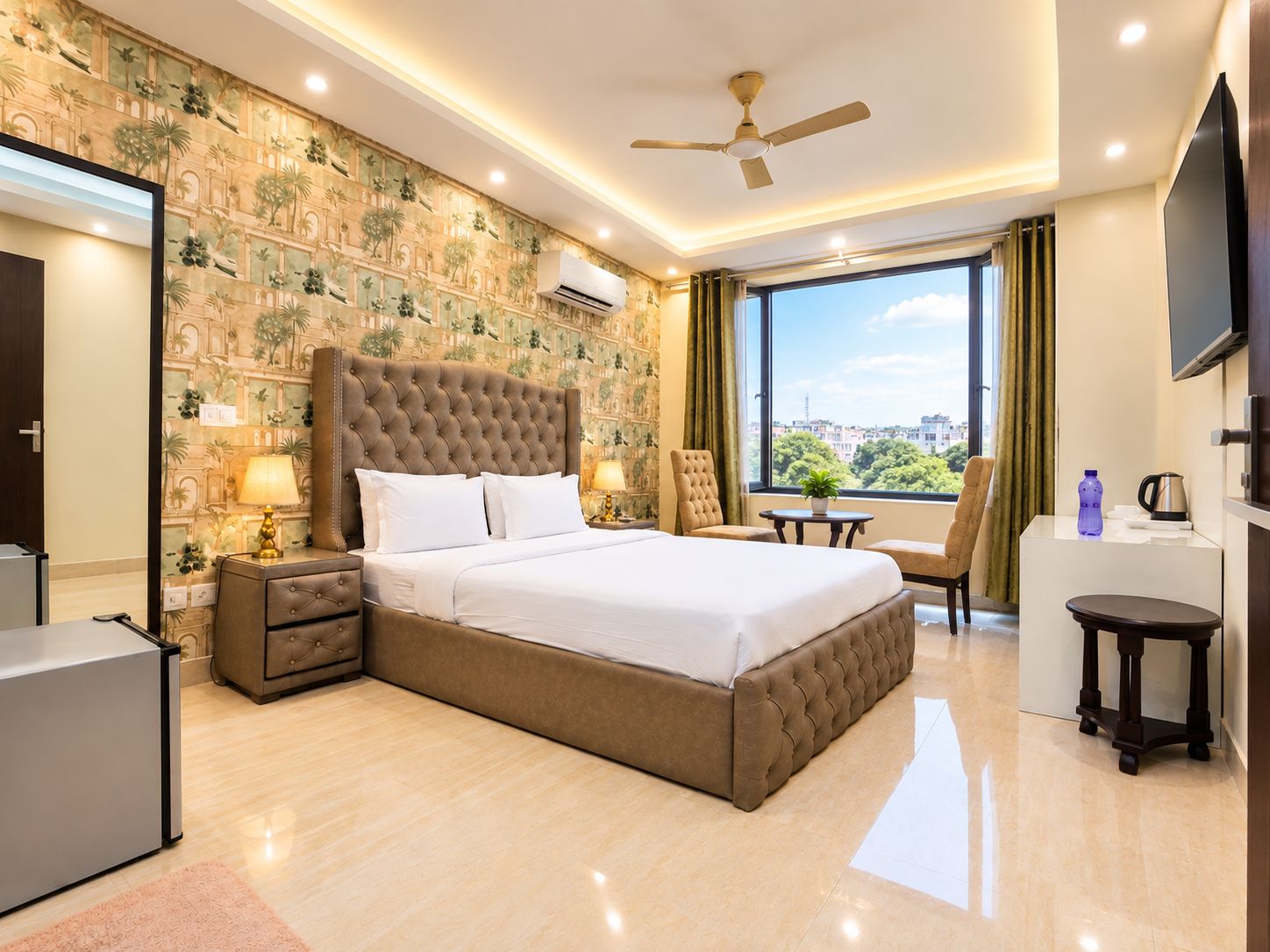 A hotel room with a large bed, a ceiling fan, a TV, and a view of the city.