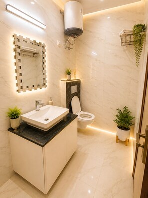 A modern bathroom with a large mirror, a sink, a toilet, and a shower area. - Ambient Express Cr Park (New Delhi)