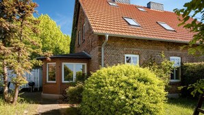 A two-story brick house with a sloped red-tiled roof, multiple windows, and a small attached garage.