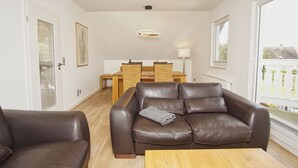 Una sala de estar moderna con un sofá de cuero marrón, una mesa de centro de madera y un comedor con mesa y sillas.