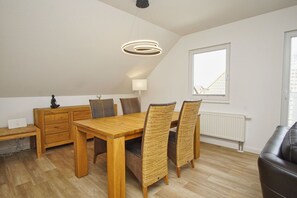 A dining area with a wooden table and wicker chairs, a small cabinet, and a ceiling light fixture.