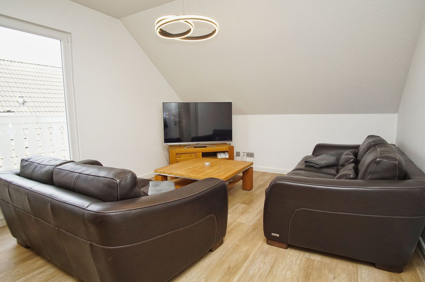 Un salon moderne avec deux canapés en cuir, une table basse en bois et un téléviseur à écran plat posé sur un meuble en bois.