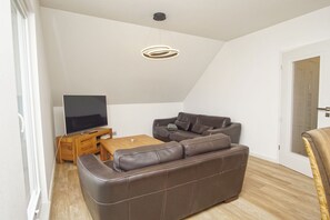 Ein modernes Wohnzimmer mit einem braunen Ledersofa, einem Holztisch und einem Flachbildfernseher auf einem Holzständer.