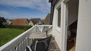 Un balcón con mesa y sillas, una terraza de madera y vistas a casas vecinas.