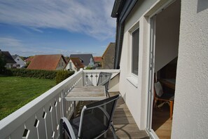 Un balcon avec une table et des chaises, une terrasse en bois et une vue sur les maisons voisines.
