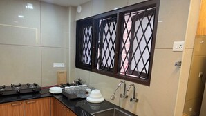 A modern kitchen with a black countertop, stainless steel sink, and wooden cabinets. - URBAN VIBES SERVICE STAY (Mangaluru)