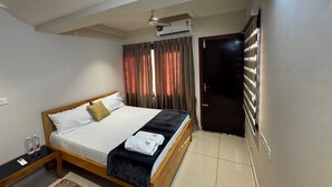 A bedroom with a bed, a bedside table, a rug, an air conditioning unit, and a door. - URBAN VIBES SERVICE STAY (Mangaluru)