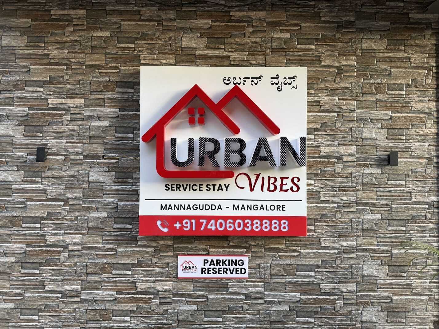 Señal para estadía Urban Vibes en Mangalore-Mysore, con número de contacto y aviso de estacionamiento reservado.