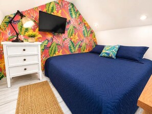 Ein Schlafzimmer mit einem Bett, einem Nachttisch, einer Lampe, einem Fernseher und floralem Wandpapier.