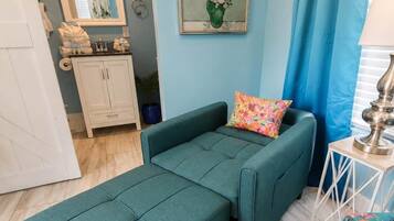 Un canapé de couleur turquoise agrémenté d’un coussin aux couleurs vives, un tableau représentant des fleurs et une petite table avec une lampe.