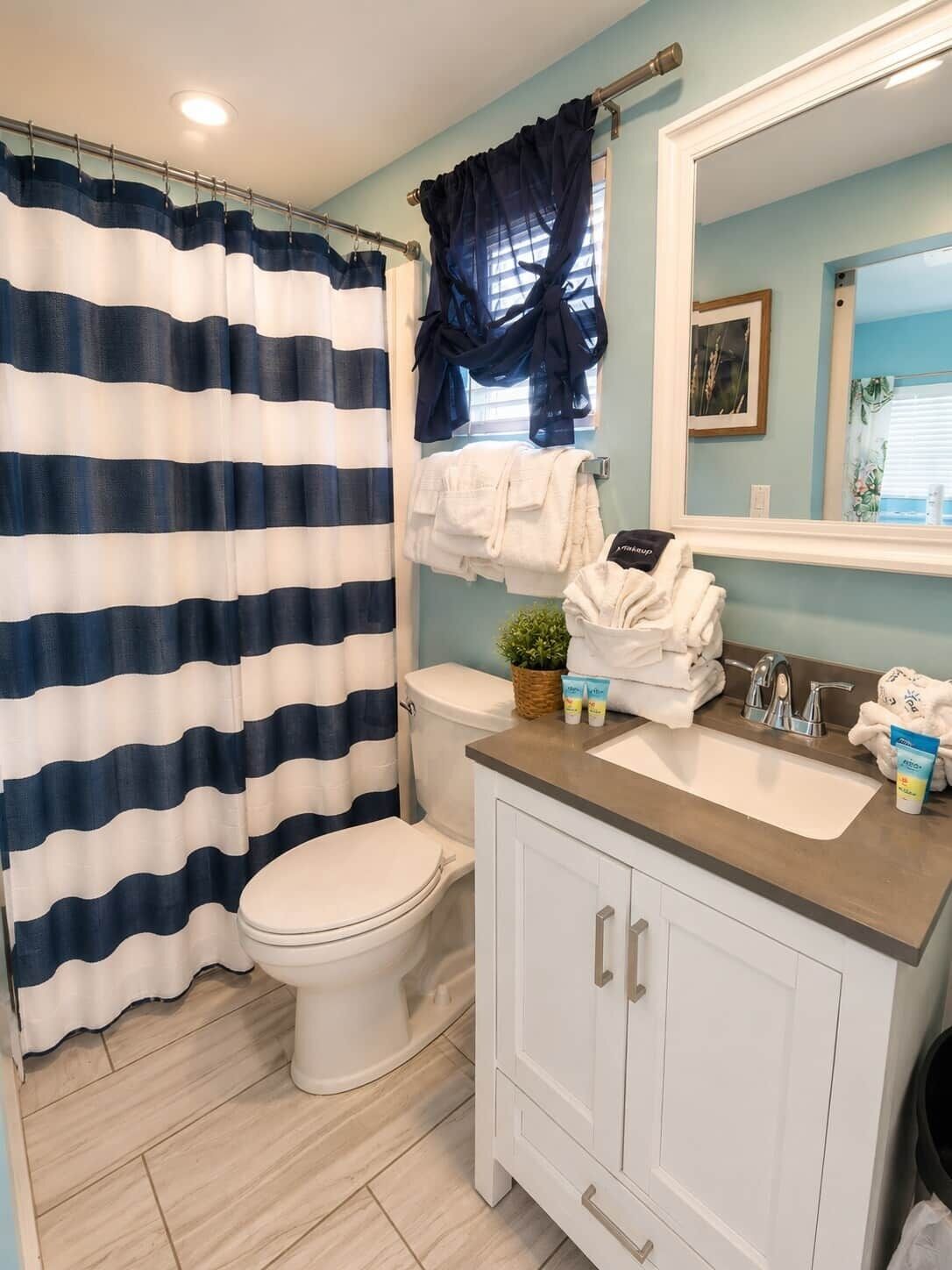 A bathroom with a striped shower curtain, a toilet, a sink with toiletries, and a mirror.
