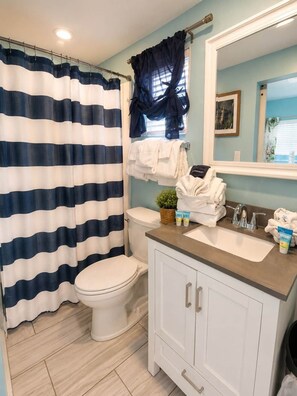 A bathroom with a striped shower curtain, a toilet, a sink with toiletries, and a mirror.