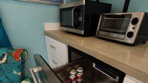 A compact kitchen with a microwave, toaster, and a built-in oven. There is a colorful floral sofa and a small cabinet above the counter.