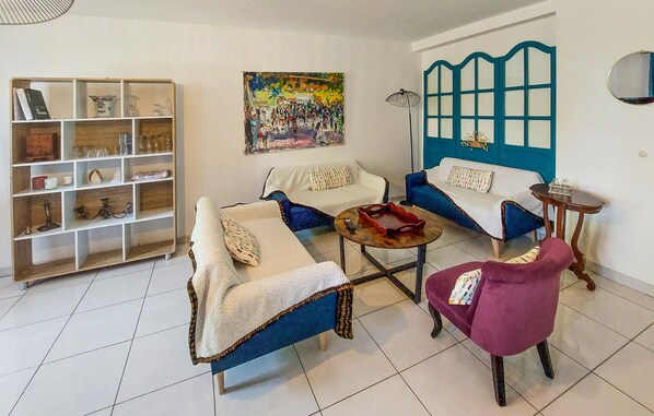 A living room with a sofa, armchair, and coffee table, a bookshelf, and a painting on the wall. - 4 bedroom amazing home in Paimboeuf (Paimboeuf)