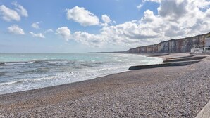 A pebbled beach with a rocky cliff and a clear sky.