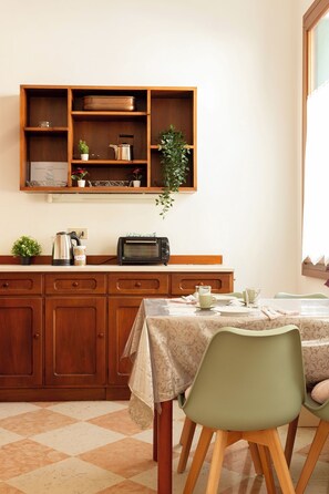 A kitchen with wooden cabinets, a microwave, a kettle, and a potted plant.