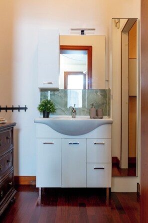 A bathroom with a white vanity, a mirror, a sink, and a potted plant.