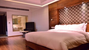 A modern bedroom with a large bed, a television, and a glass-enclosed bathroom. - Hotel Silvete (Lucknow)