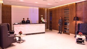 A reception area with a reception desk, two staff members, a man in a suit, and a modern interior design. - Hotel Silvete (Lucknow)