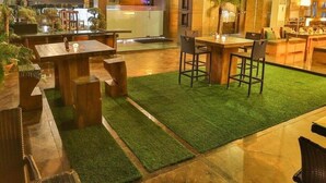 An outdoor seating area with tables and chairs, a grassy lawn, and a building with a glass facade. - Hotel Silvete (Lucknow)