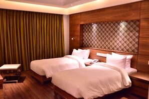 A hotel room with two beds, a wooden headboard, a small table, and a curtain.