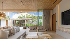 Una sala de estar moderna con un sofá, una mesa de centro y sillas, un televisor montado en la pared y un ventanal con vistas a un jardín.