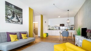 A modern living room with a sofa, a yellow armchair, a dining area with a kitchen in the background, and a large painting on the wall.